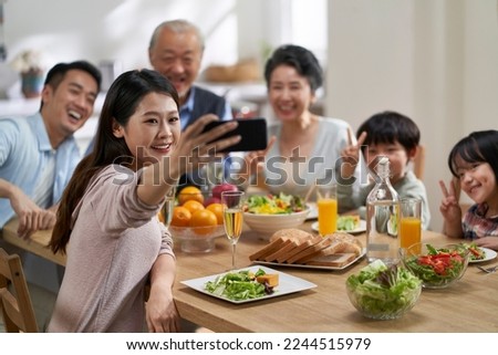 three generational asian family taking a selfie while having meal together