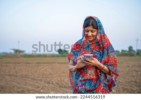 Indian rural woman in traditional saree and using smartphone at agriculture field. Royalty-Free Stock Photo #2244516319