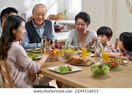 young asian woman sharing pictures in cellphone with three generation family while eating meal together