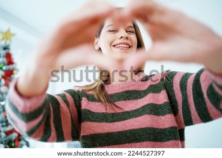 Happy - cheerful beautiful girl in a bedroom decorated in Christmas theme, lovely cute girl making a hands sign in hearth shape and smiling to camera.