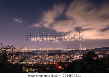 A vibrant cityscape with white clouds moving in the night sky. Night view of the city surrounded by mountains is hazy and dreamy.. Taipei City, Taiwan