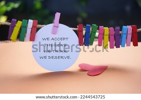 Life inspirational and motivational quote - We accept the love we think we deserve. On colorful background of white circle notepaper, red heart falling and wooden clips on rope. Self love care concept