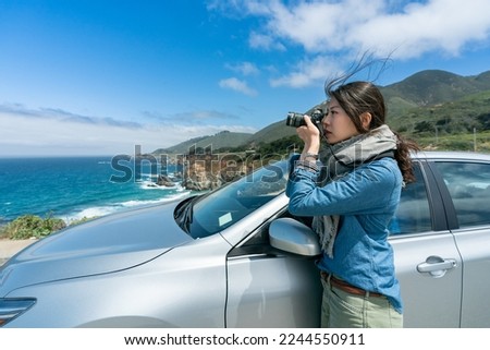 side portrait of asian chinese professional woman photographer on California road trip taking pictures of scenery at seaside with slr camera by her car