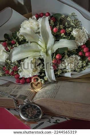 Golden heart shaped padlock lock placed on old book and Vintage pocket watch in front of with Beautiful bouquet of flowers background. Symbol of Romantic forever love, Valentine's day concept.