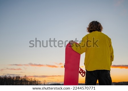 Snowboarder holding a snowboard on top of the mountain and looking reflecting into a distance. Winter holidays.