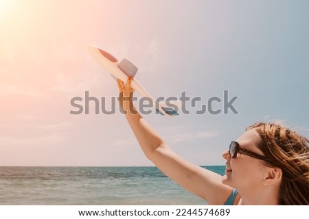 Woman hand holding toy airplane on blue sky and white clouds at sunset sea beach abstract background. Travel adventure and freedom concept.