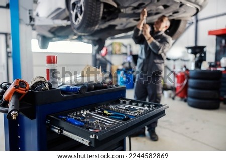 Cropped picture of a mechanic toolbox with tools in drawer with worker repairing car in blurry background at workshop.