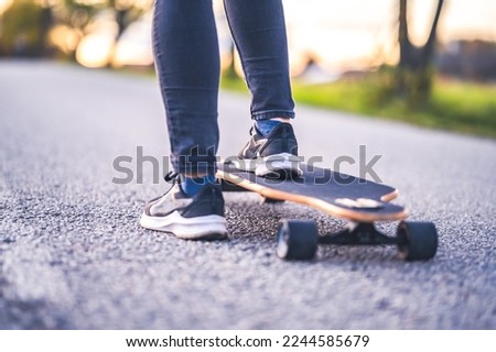 Woman rides at straight road on longboard at sunset time. Skater in casual wear training on board during evening sunset with orange light. Girl hold longboard in hands