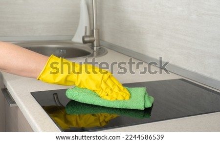Cleaning Black shiny surface of cooker, kitchen top, hands, detergent. Deep Cleaning service. Cleaning service worker in rubber protective cleaning and polish electric cooker. Royalty-Free Stock Photo #2244586539
