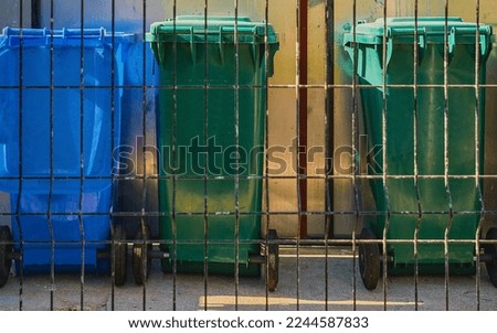 Garbage multi-colored outdoor plastic bins behind a metal grate, outdoor bins for separating waste from recycled materials.