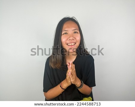 Smiling young Asian woman gesturing traditional greeting isolated over gray background