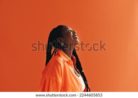 Sideview of a young black woman smiling in a studio. Woman with makeup standing against an orange background. Royalty-Free Stock Photo #2244605853