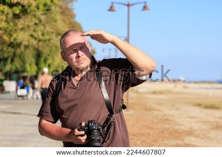 adult man makes a photo on a camera with a large lens. Near sea in the public places on a sunny day in summer