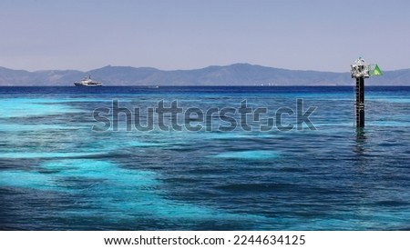 Starboard marker beacon, hydrographic survey ship and fast-going tourist motorboat seen from the Green Island-Wunyami mooring jetty, the shoreline north of Cairns as background. Queensland-Australia. Royalty-Free Stock Photo #2244634125