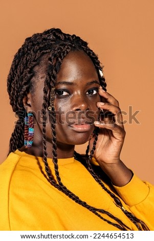 Stock photo of confident black woman with braids posing in studio shot against brown background.