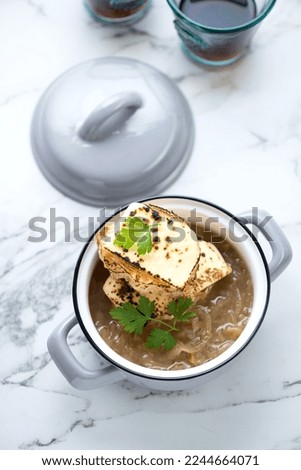 Grey serving pan with french onion soup on a white marble background, high angle view, vertical shot
