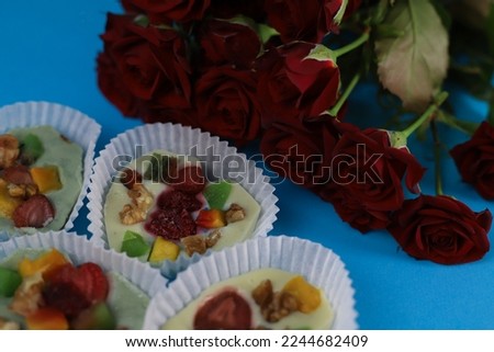 chocolate hearts made of white black milk and pistachio chocolate with fruit filling kiwi raspberry strawberry nuts and mango in muffin tins on a blue background. for screensavers labels business card