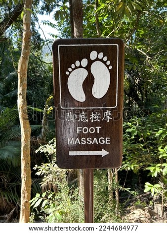 Direction to go FOOT MASSAGE at country park in Hong Kong.  A natural wooden board engraved with bare feet and word “FOOT MASSAGE” in Chinese and English letters.  White print on the picture and text.