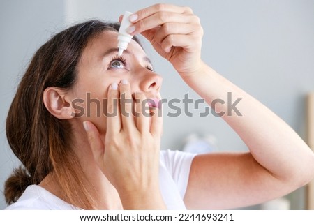 Young woman putting eye drops at home  Royalty-Free Stock Photo #2244693241