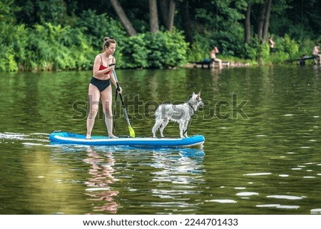 Sportive woman paddling on sup board with her funny white dog