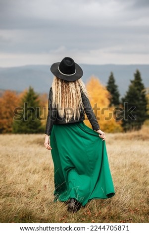 Happy, rear view of a blonde girl.  Young romantic woman in long, silk, green dress on the mountain side. Autumn season. 