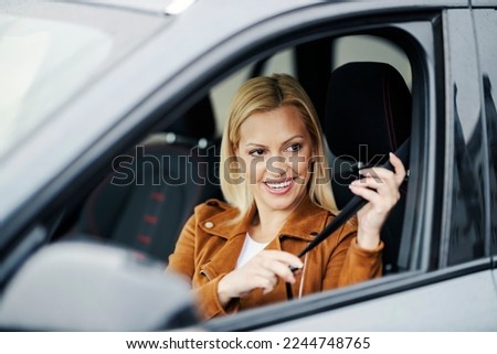 A happy woman is sitting in car and buckling seat belt. Royalty-Free Stock Photo #2244748765