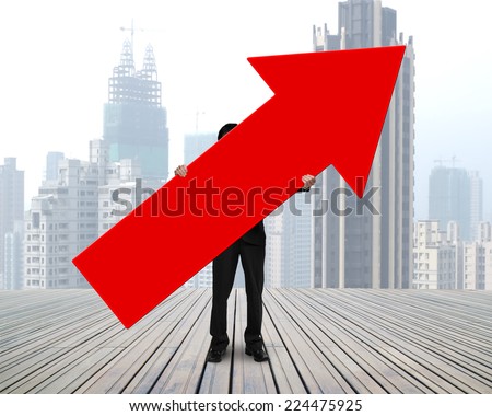 standing businessman holding red arrow sign on wooden floor with cityscape background