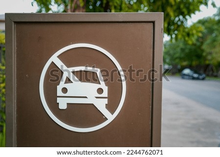 Do not parking sign with brown and white color stand in the village, with black a car blurred in the background.