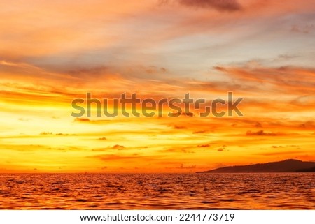 the tip of the island as seen from the ocean when the sun is about to set in eastern Indonesia with a sky full of yellowish-orange colors and their reflections on the surface of the sea Royalty-Free Stock Photo #2244773719