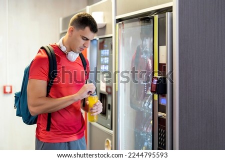 Athlete in gym consuming drink from food vending machine Royalty-Free Stock Photo #2244795593