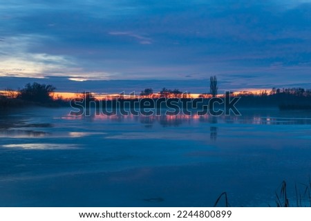 Winter landscape of a frozen pond. Blue hour after sunset. Beautiful clouds and frozen pond surface.