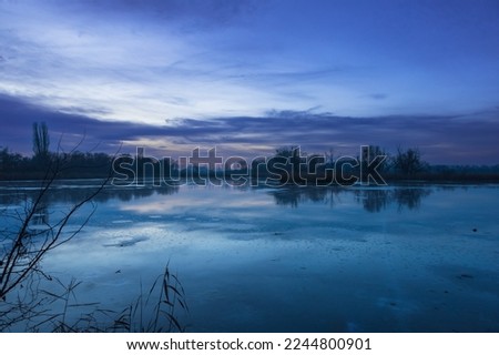 Winter landscape of a frozen pond. Blue hour after sunset. Beautiful clouds and frozen pond surface.