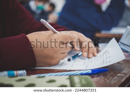 University student holding pen or pencil writing on paper answer sheet sitting on chair lecture final exam participates in exam room or classroom in uniform student Royalty-Free Stock Photo #2244807351