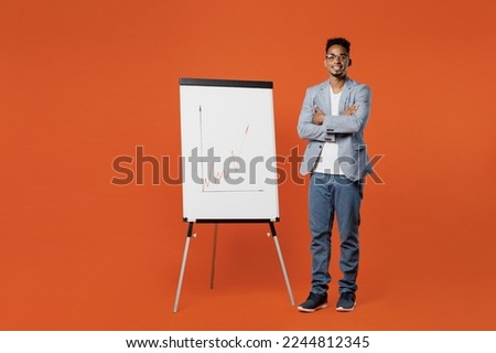Full body fun young employee business man corporate lawyer wear classic formal grey suit shirt glasses work in office use flipchart show graph on marker board isolated on plain red orange background Royalty-Free Stock Photo #2244812345