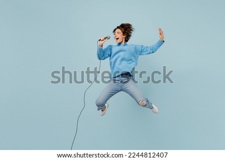 Full body young singer happy woman wear knitted sweater jump high sing song in microphone raise up hand isolated on plain pastel light blue cyan background studio portrait. People lifestyle concept Royalty-Free Stock Photo #2244812407
