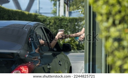 Hand Man in car receiving coffee in drive thru fast food restaurant. Staff serving takeaway order for driver in delivery window. Drive through and takeaway for buy fast food for protect covid19.