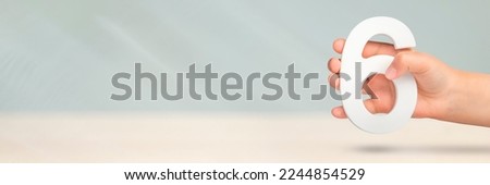 Number six in hand. Hand holding white number 6 on blurred background with copy space. Concept with number six. Birthday 6 years, sixth grade. Royalty-Free Stock Photo #2244854529