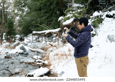 Man is taking a picture during winter and snowing. 
