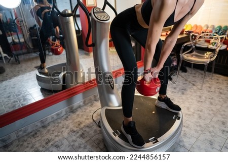 Unknown woman hold red kettlebell weight while standing on power plate vibration platform machine during training workout squat exercise copy space Royalty-Free Stock Photo #2244856157