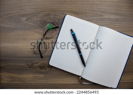 Blank checkered notepad, glasses and pen placed on wooden background