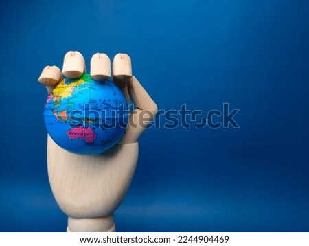 Wooden hand holding earth globe on a blue background.