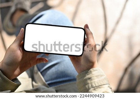 Above view, A female holding a smartphone in horizontal position, watching video, playing mobile game. phone white screen mockup Royalty-Free Stock Photo #2244909423