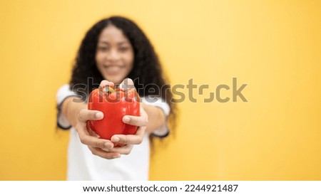 Young satisfied happy African American woman 20s in casual look camera hold red bell peppers isolated on plain yellow background studio portrait. People lifestyle food concept