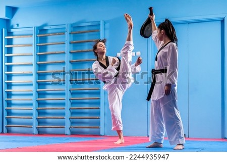 Portrait of two young women in kimono and suture, taekwondo athletes wrestling in the gym. Sportswomen demonstrating taekwondo martial art, hard training concept