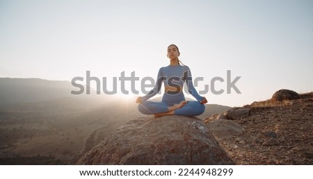 Fit girl doing lotus pose. Young athletic woman meditating in mountains, training and relaxing during sunrise - active lifestyle, zen concept  Royalty-Free Stock Photo #2244948299