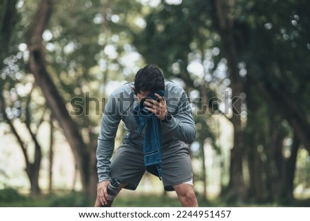 a tired young man resting and breathing holding a bottle of drinking water and towel on the road in the park morning. Royalty-Free Stock Photo #2244951457