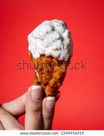 Hand holding a chicken wing with buffalo and ranch dressing on a red background. Royalty-Free Stock Photo #2244956419