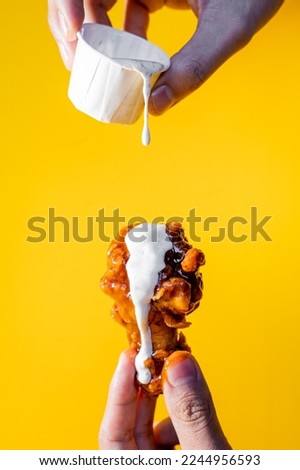 Hand holding a chicken wing with buffalo and ranch dressing on a yellow background. Royalty-Free Stock Photo #2244956593