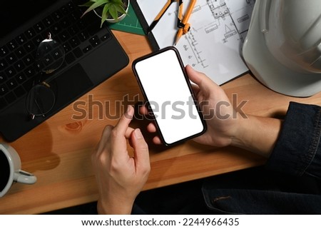 Engineer man hands holding smart phone over his workstation. Top view, blank screen for your advertise Royalty-Free Stock Photo #2244966435