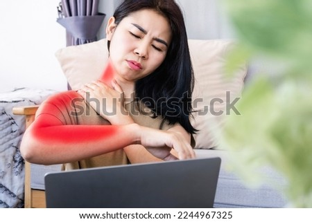 Asian woman suffering from neck pain spreading to shoulder and down arm caused by overworked on a computer with bad posture 